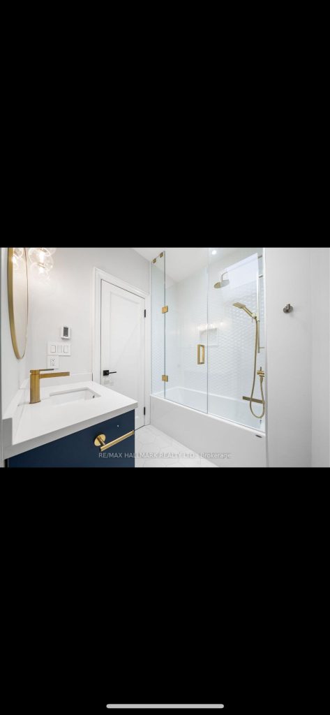Toronto bathroom remodel featuring a navy blue vanity with gold faucet, white countertop, frameless glass tub-shower combo with gold hardware, and modern finishes.