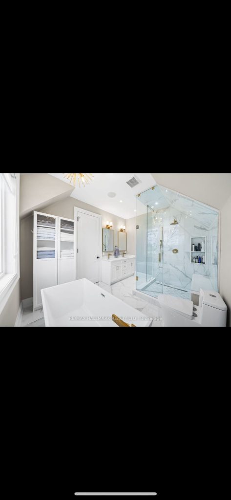Elegant white marble bathroom with double sink vanity, frameless glass shower with gold fixtures, built-in shelving, and contemporary lighting.